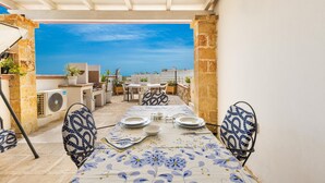Une terrasse sur le toit, avec une table dressée pour les repas, des sièges d’extérieur et une vue sur la mer.