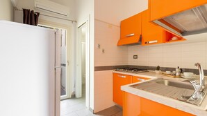 A kitchen with orange cabinets, a stainless steel sink, and a white refrigerator. - 2668 Casa Conchiglia (Gallipoli)