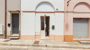 A building with a white facade, a central arched doorway, and a closed shutter on the right. - 2380 Casa Crispi (Alezio)
