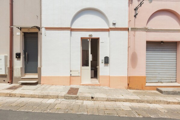 A building with a white facade, a central arched doorway, and a closed shutter on the right. - 2380 Casa Crispi (Alezio)
