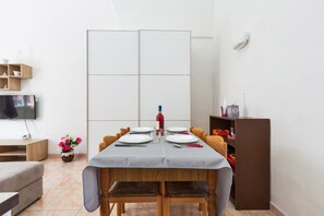 A dining area with a table set for four, a television on the left, and a bookshelf with toys on the right. - 2380 Casa Crispi (Alezio)