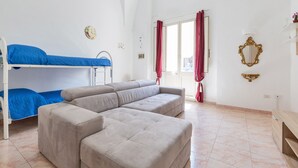 A room with a bunk bed, a grey sofa, a small table, and a mirror on the wall. - 2380 Casa Crispi (Alezio)