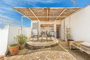 Une terrasse sur le toit, avec une table et des chaises, entourée de plantes en pot et d’un banc.
