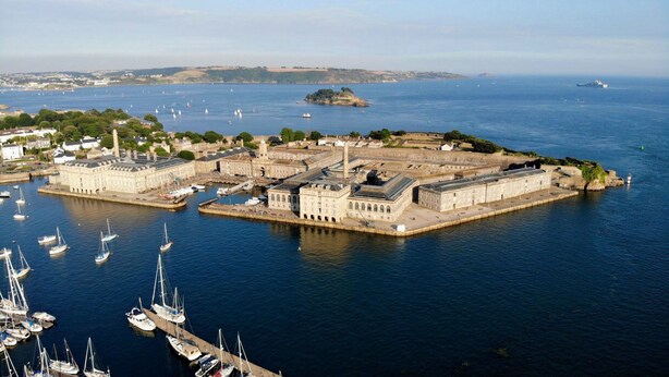A coastal town with a historic fort, a marina with sailboats, and a distant island.