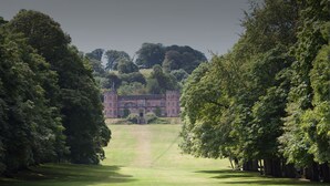 A large, historic building with a symmetrical facade, surrounded by lush greenery and a well-maintained lawn.