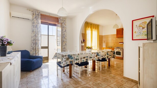 A living room with a blue sofa, a dining table with a patterned tablecloth, and a kitchen visible through an archway. - 2967 Dimora di Lucia by Barbarhouse (Taviano)