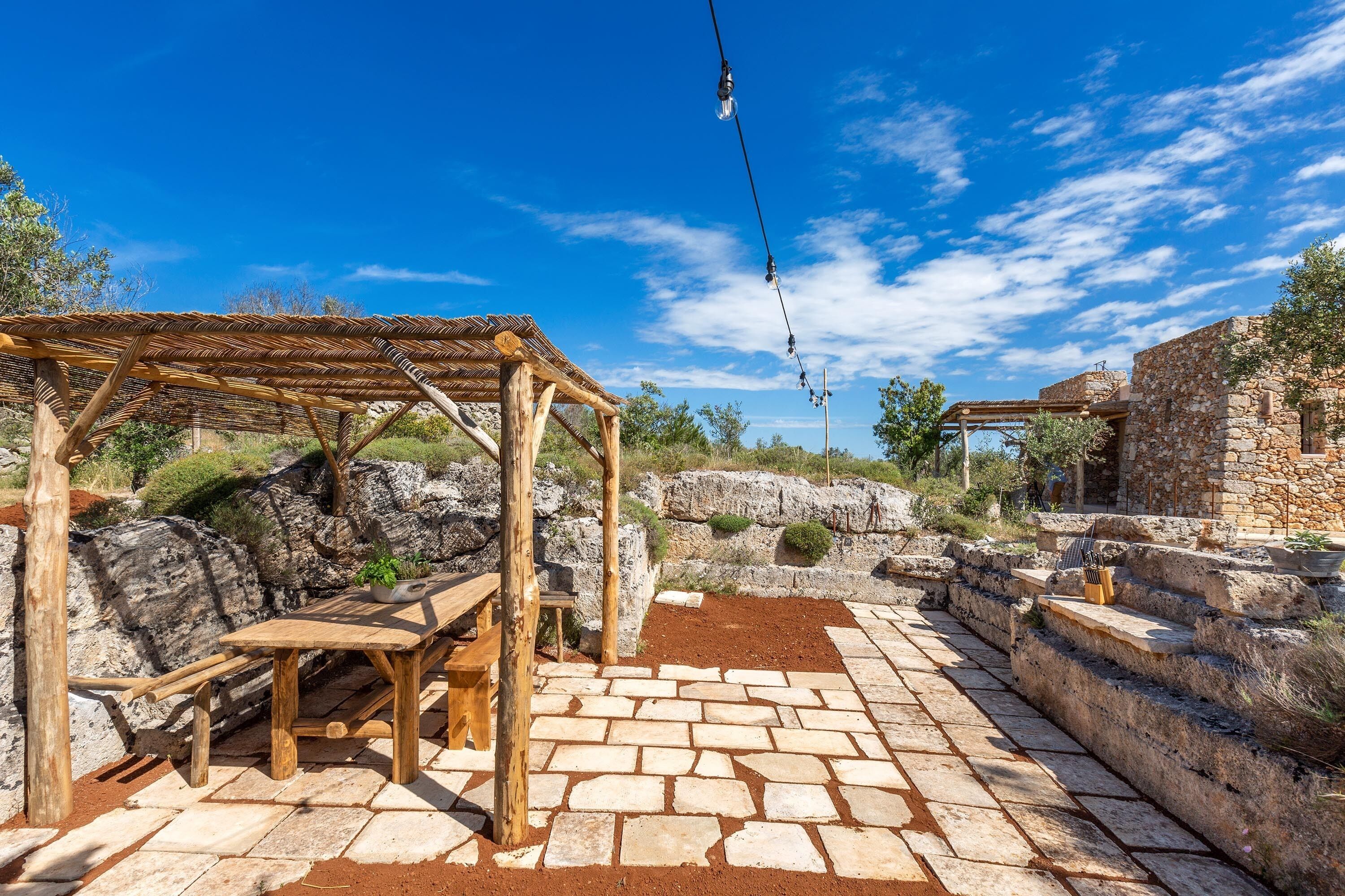 Une terrasse extérieure dotée d’un sol en pierre, de meubles en bois et d’une structure en forme de pergola.