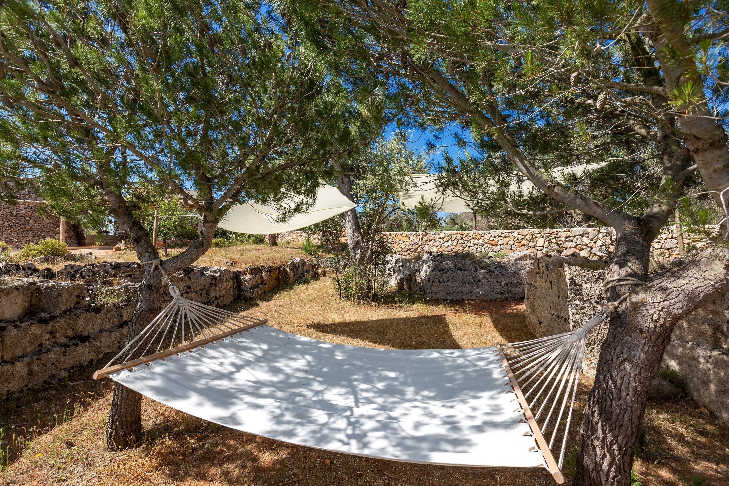 A hammock between trees in a garden with stone walls and a stone building in the background.