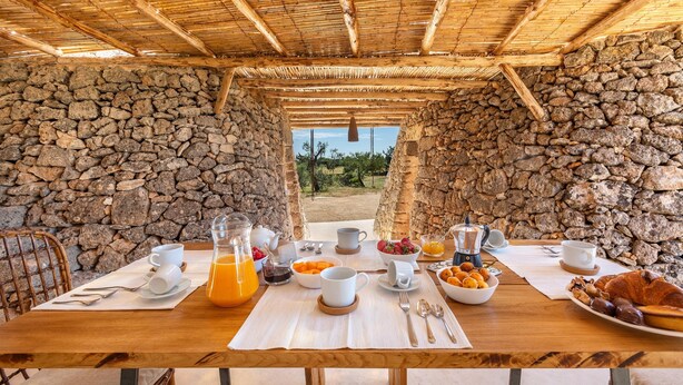 A breakfast setup with stone walls, a wooden table, and a view of the outdoors.