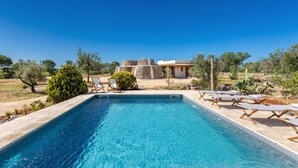 A swimming pool with lounge chairs, surrounded by greenery and a stone building in the background.