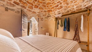 A bedroom with a stone ceiling, a bed with striped bedding, a wooden wardrobe, and a clothing rack with various garments.