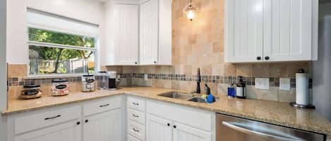 A modern kitchen with white cabinets, a granite countertop, a stainless steel dishwasher, and a window providing natural light.