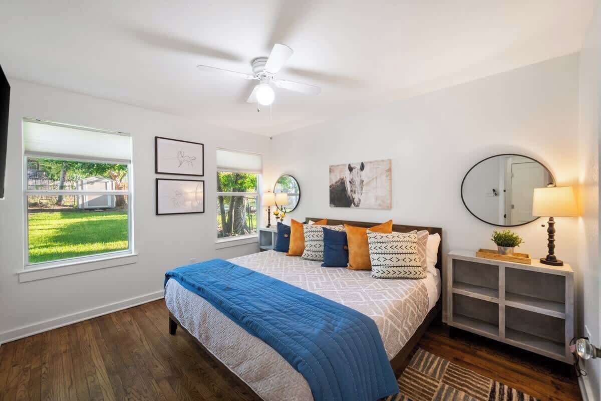 Une chambre à coucher avec un lit, un ventilateur de plafond, une fenêtre, une table de chevet et un miroir.