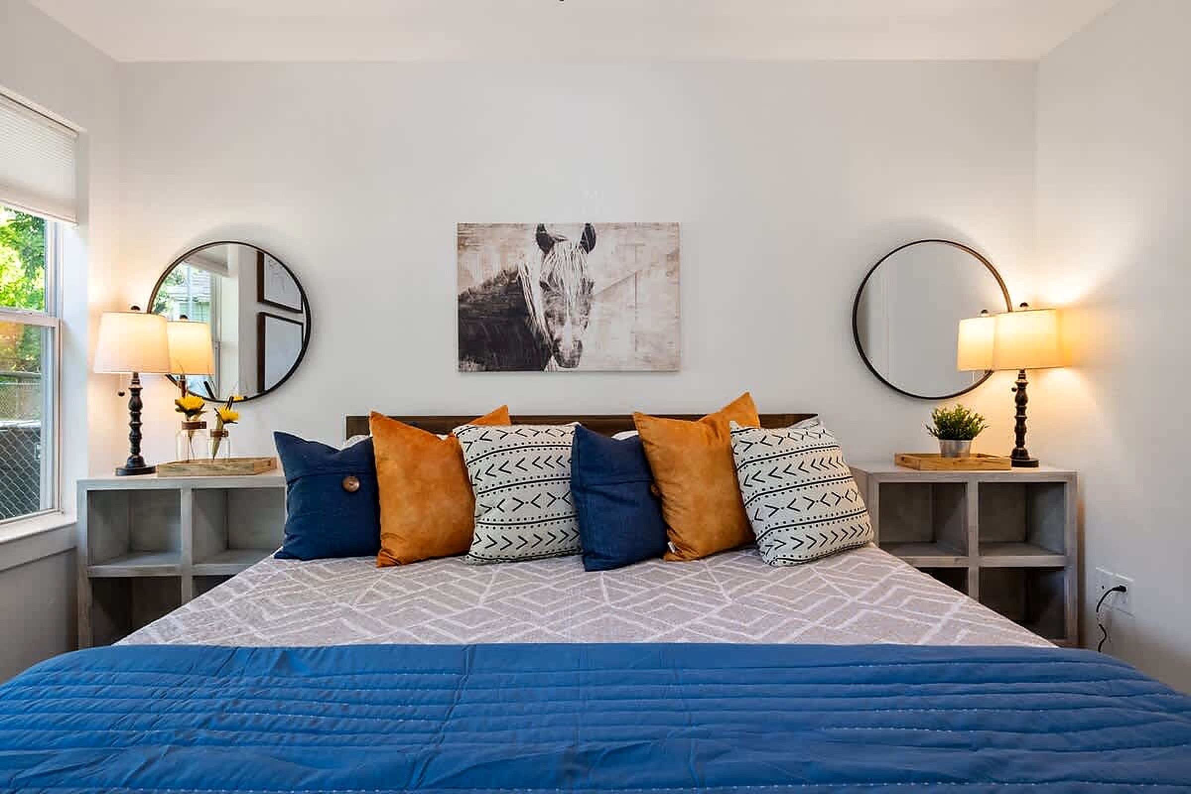 Een slaapkamer met een bed, twee nachtkastjes, een spiegel, een kunstwerk aan de muur en een raam.