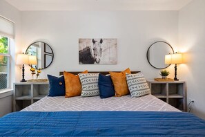 A bedroom with a bed, two bedside tables, a mirror, a wall-mounted artwork, and a window. - Walk to Dickies Arena · 3BR Near TCU · Fenced Yard (Fort Worth)