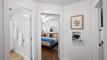 Ein Flur, der zu einem Schlafzimmer führt, mit einem Bett, einem Spiegel und einem gerahmten Bild an der Wand.