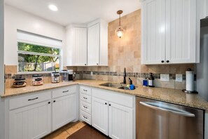 A modern kitchen with white cabinets, a stainless steel dishwasher, and a window overlooking a garden. - Walk to Dickies Arena · 3BR Near TCU · Fenced Yard (Fort Worth)