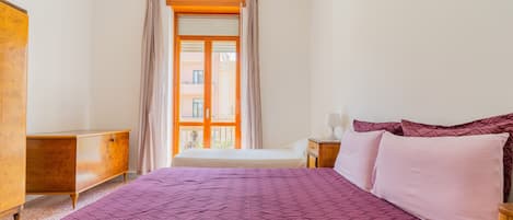 A bedroom with a large bed, a wooden dresser, and a window with curtains.