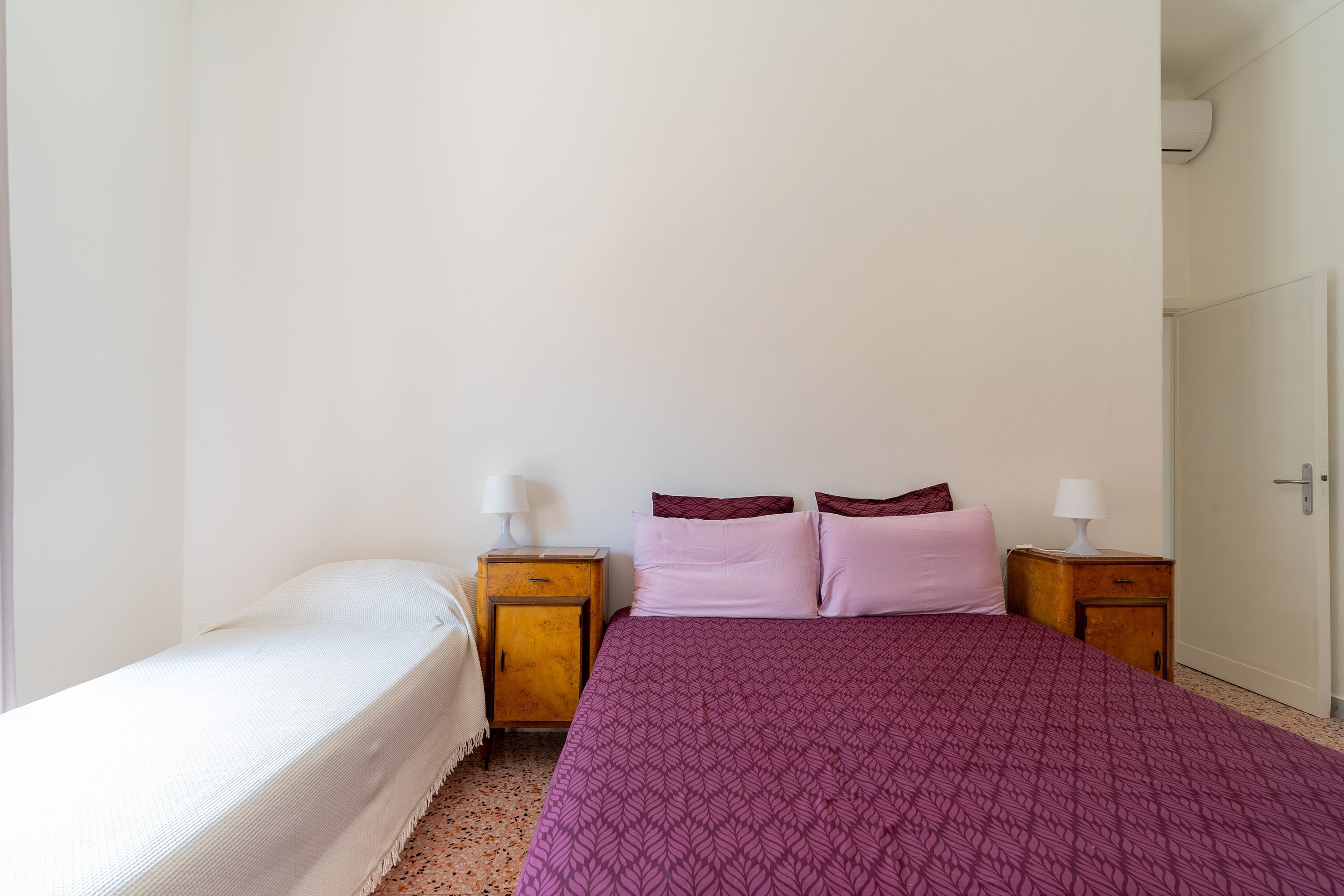 A bedroom with a single bed, a nightstand with a lamp, and a door.