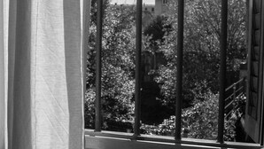 Une fenêtre avec un garde-corps en métal, des rideaux et une vue sur des arbres et des immeubles.