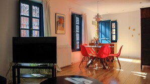 Un salon moderne doté d’un téléviseur à écran plat, d’un coin repas avec des chaises rouges et de grandes fenêtres avec des volets bleus.