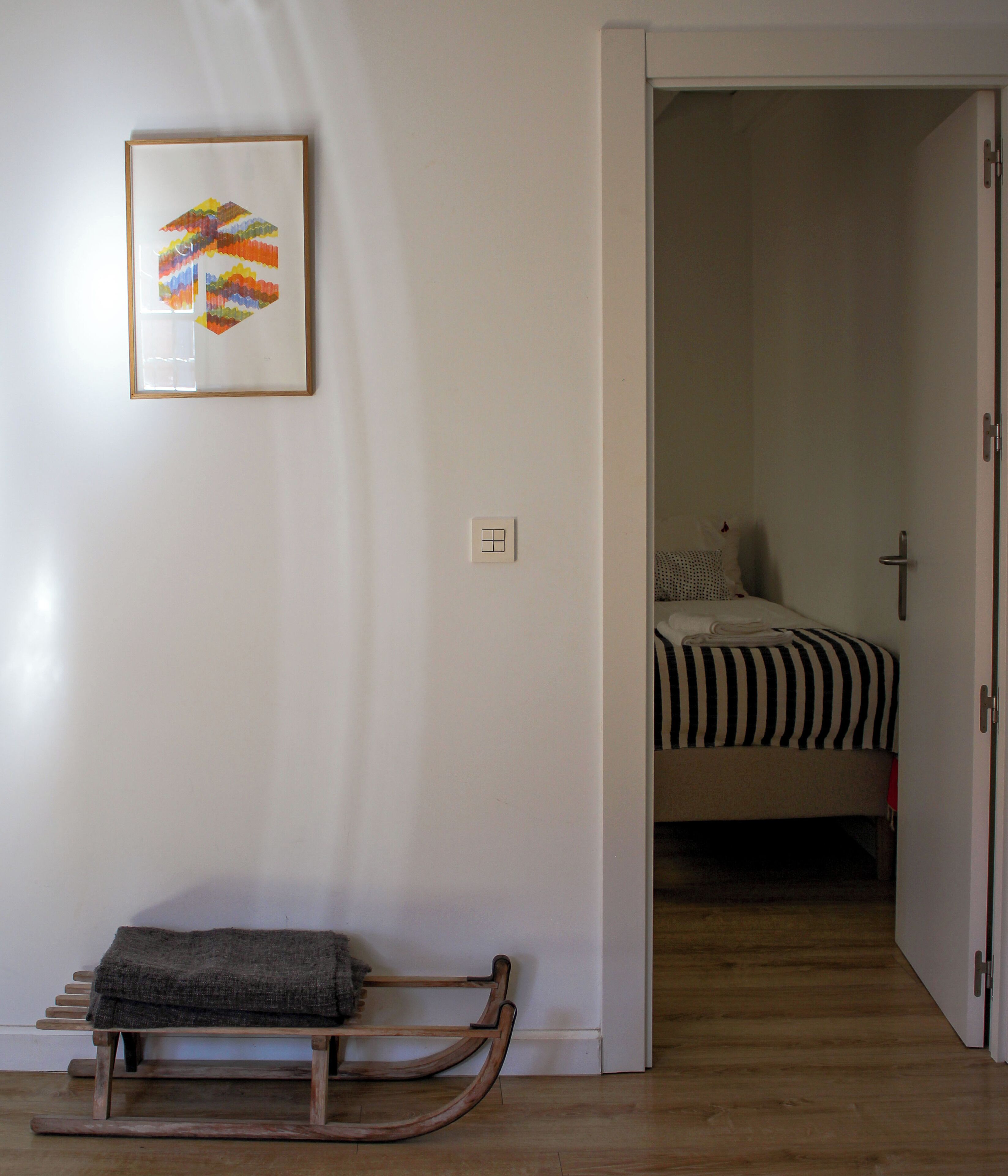 A room with a wooden bench, a bed with striped bedding, and a colorful artwork on the wall.