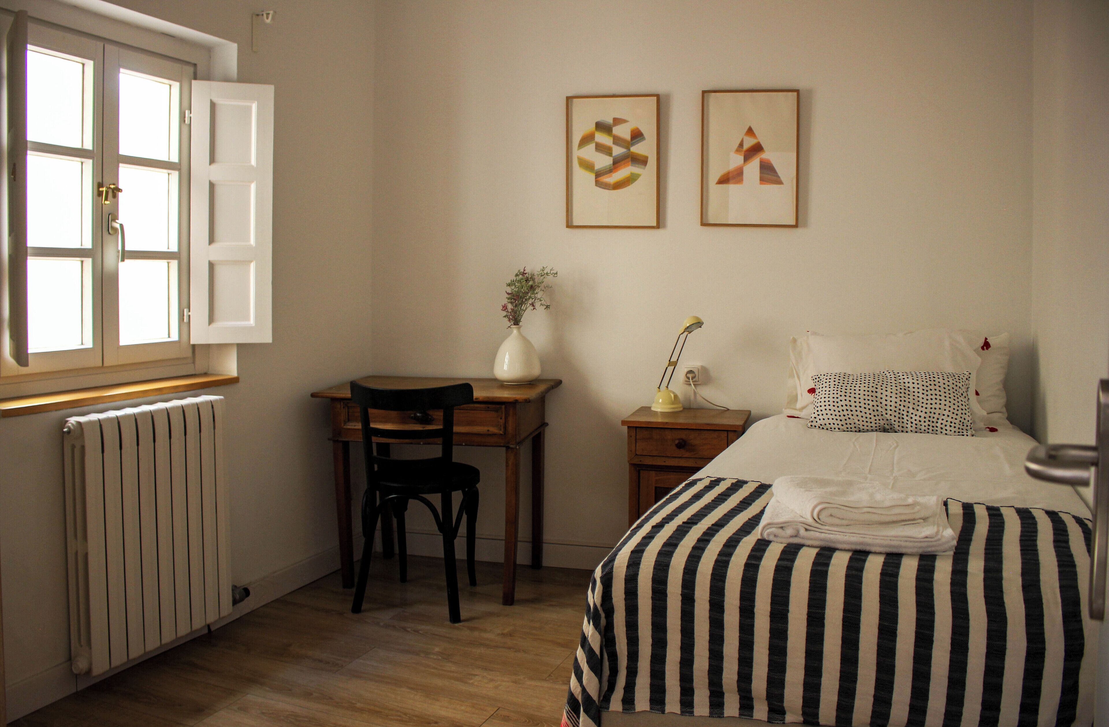 Ein Schlafzimmer mit einem Bett, einem Schreibtisch, einem Stuhl, einer Heizung und zwei gerahmten Bildern an der Wand.
