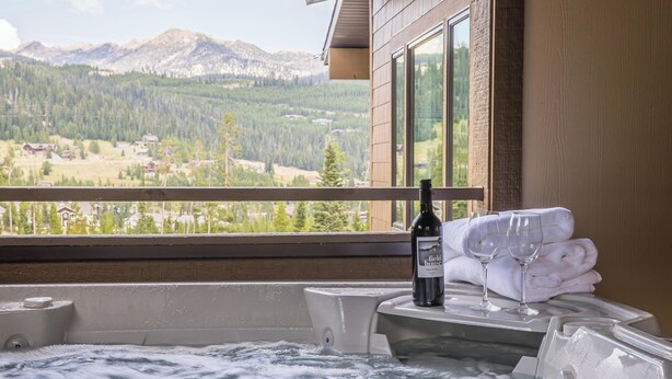 A hot tub with a bottle and glasses, a window with a mountain view, and a wooden wall. - Luxury Ski In/Out ᨒ Beaverhead Condo | Hot Tub | 10 Min Walk to Resort (Big Sky)
