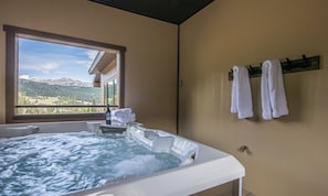 Un baño con bañera de hidromasaje, toallas en un perchero y una ventana con vistas a la montaña.