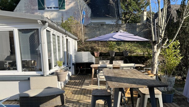 Ein Außenbereich mit Terrassenausstattung, Holztafeln und -stühlen, einem Grill und Blumentöpfen.