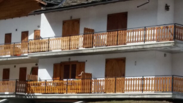 A multi-story building with balconies, wooden railings, and a snow-covered ground. - Holidays on the lake (Valtournenche)