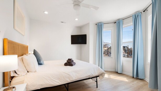 Une chambre dotée d’un lit, d’un téléviseur à écran plat, d’un ventilateur de plafond et offrant une vue sur la ville grâce à de grandes fenêtres.