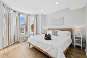 A modern hotel room with a large bed, white linens, a wooden headboard, and a view of the city.