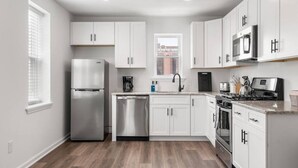 A modern kitchen with white cabinets, stainless steel appliances, and a wood floor.