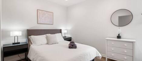 Un dormitorio con cama, mesitas de noche, cómoda, ventilador de techo y espejo en la pared.