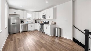 A modern kitchen with white cabinets, stainless steel appliances, and a wooden floor.