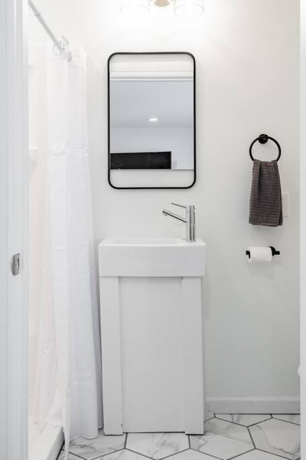 A bathroom with a white sink, a mirror, a towel ring, and a toilet paper holder.