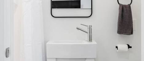A bathroom with a white sink, a mirror, a towel ring, and a toilet paper holder.