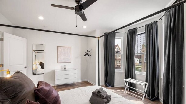A modern bedroom with a bed, a dresser, a ceiling fan, and a view of the outside.