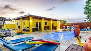 Ein Garten mit Schwimmbecken, Liegestühlen und einer überdachten Terrasse.