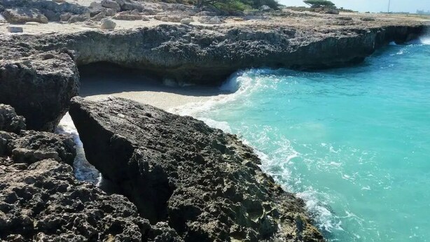 Eine felsige Küstenlinie mit klarem türkisblauem Wasser und einer schmalen Passage zwischen großen Felsen.