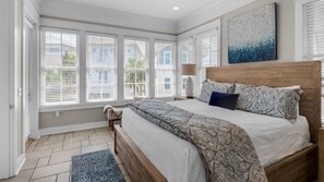 A bedroom with a large bed, a nightstand, a lamp, and a window with blinds. - Splash Pool, Carriage House, Free Beach Chair Setup & Attraction Tickets! (Panama City Beach)