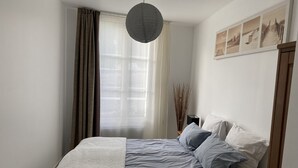 Une chambre à coucher avec un lit, une table de chevet, une lampe et une fenêtre avec des rideaux.