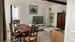 Un coin repas avec une table et des chaises en bois, un téléviseur posé sur un meuble, une plante en pot et un buffet.