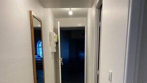 Un couloir étroit au sol carrelé, un miroir à cadre en bois et une porte donnant sur une pièce faiblement éclairée.