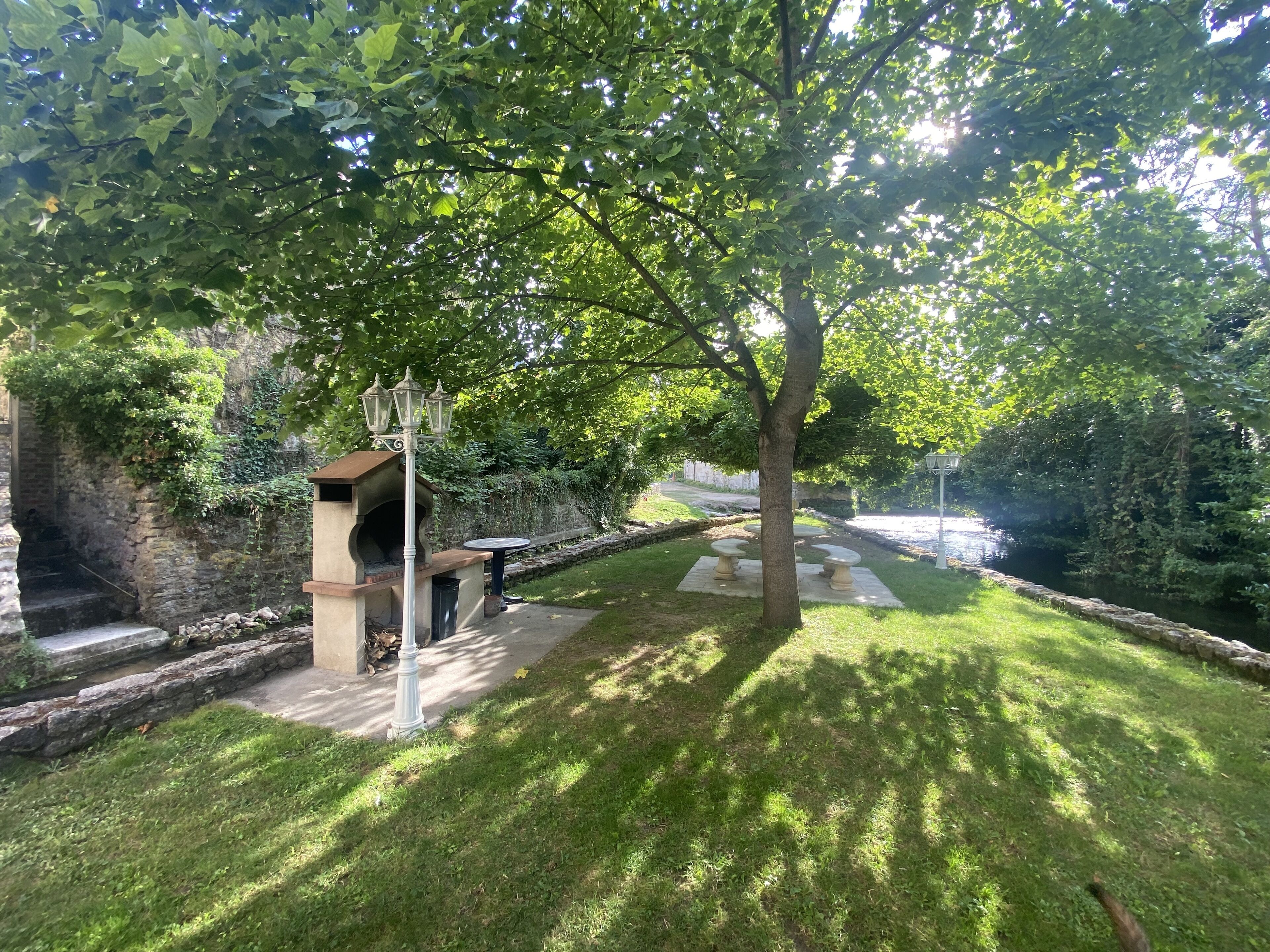 A stone-built outdoor area with a grill, a lamp post, and a paved path alongside a water feature.