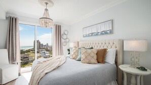 A bedroom with a large bed, a view of the city, a chandelier, and a painting on the wall. - Sandestin, Gulf Front Condo, Golf Cart (Miramar Beach)