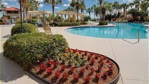 A pool area with a circular flower bed and palm trees in the background. - Sandestin, Gulf Front Condo, Golf Cart (Miramar Beach)