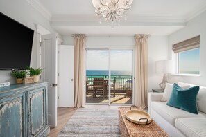 A living room with a television, a sofa, a coffee table, and a view of the ocean through a sliding door. - Romancing the Beach, Sandestin, Gulf Front Condo, Golf Cart (Miramar Beach)