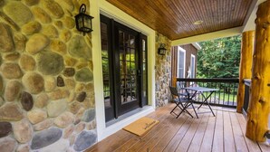 Eine Mauer aus Stein, eine Holzterrasse und eine Tür mit schwarzen Fensterläden.
